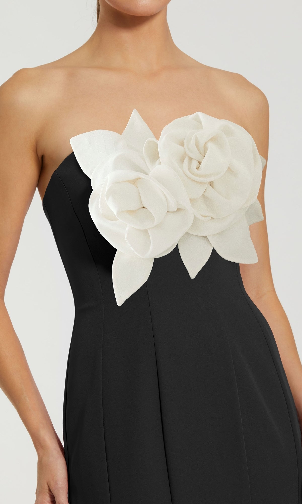 A woman wears the Mac Duggal 2300, a strapless long black formal dress with two large white flower appliqués on the bodice.